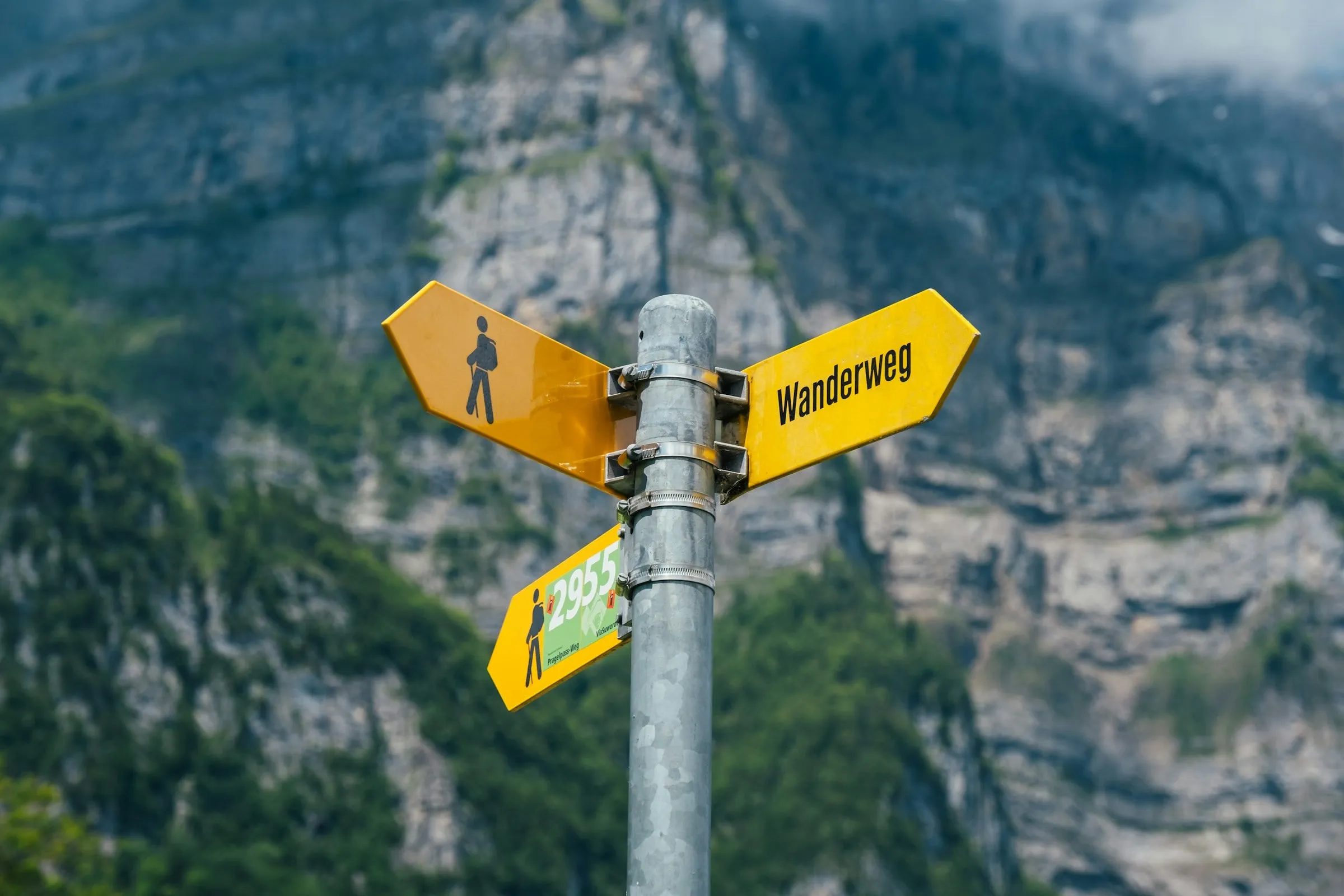 Gelbe Wanderwegweiser an einem Mast vor einer Felswand im Kanton Glarus